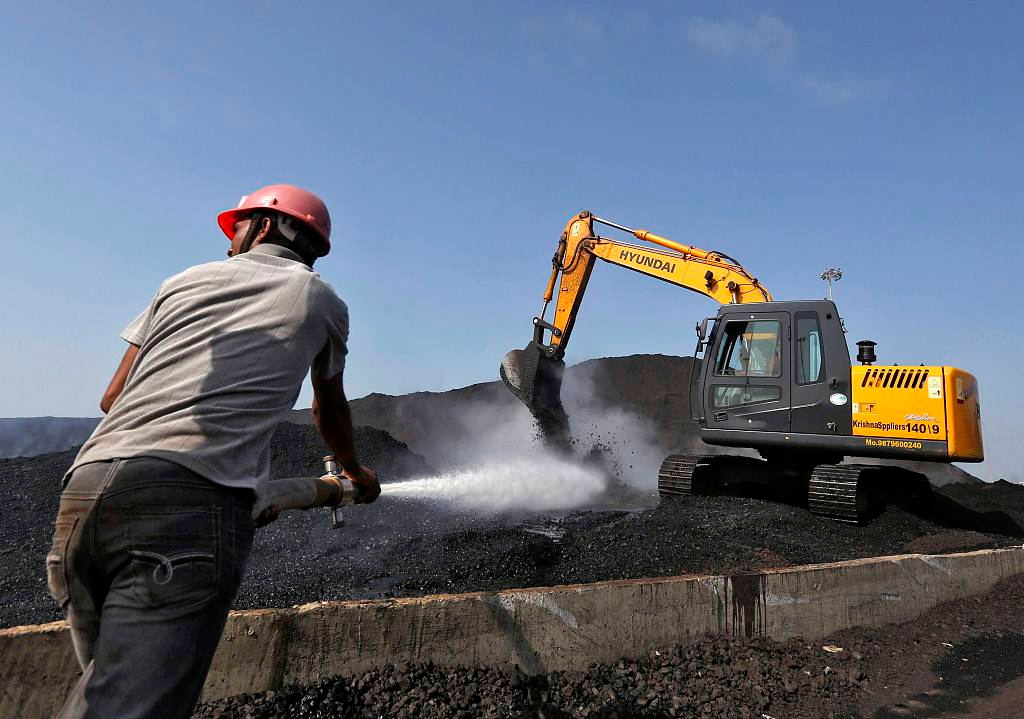 A worker sprays water over piles of coal as a bulldozer shifts coal at Mundra Port Coal Terminal in the western Indian state of Gujarat April 2, 2014. [Photo/IC]