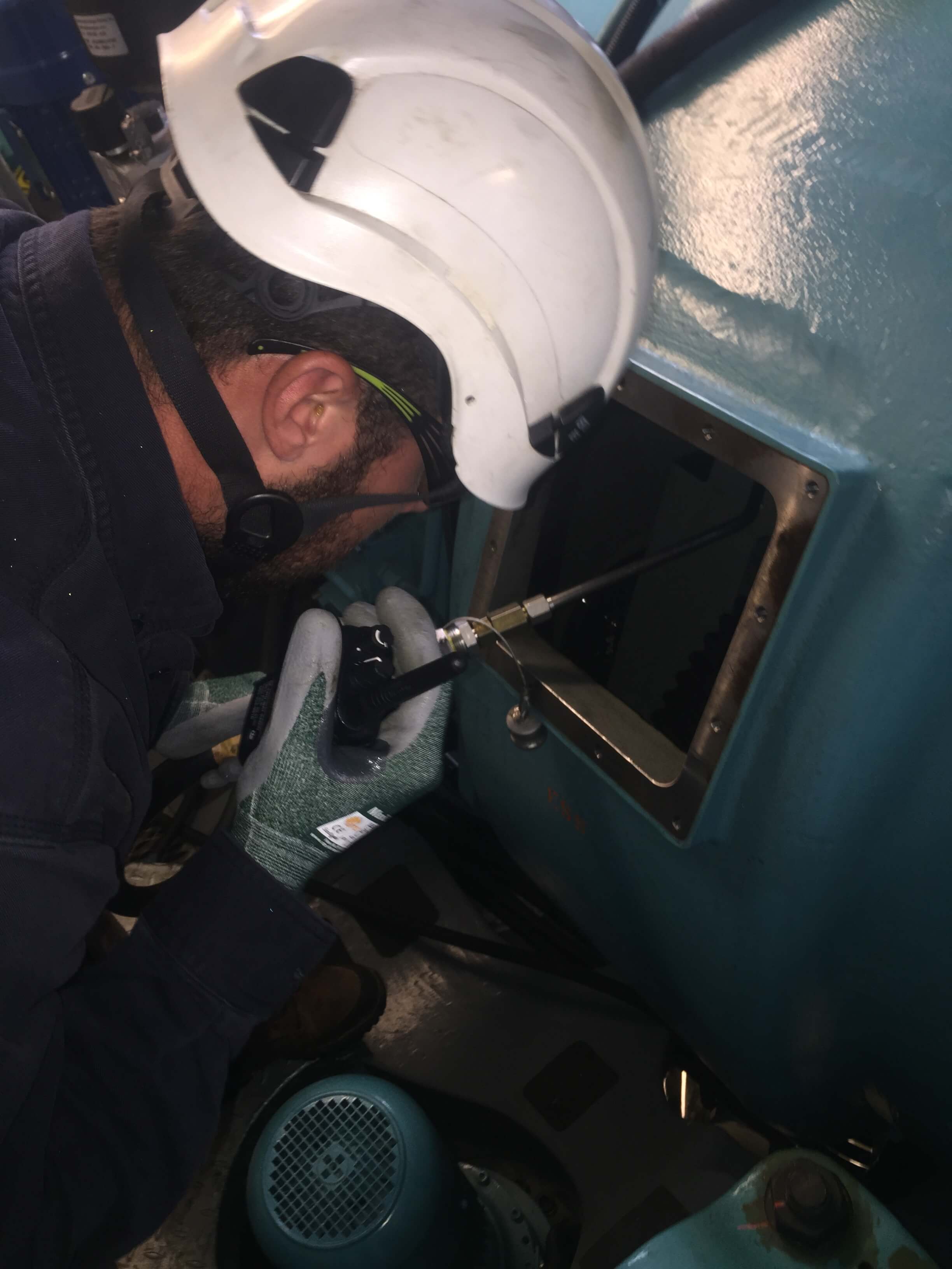 A wind tech sprays down the high-speed helical section of a wind-turbine gearbox during an oil change.