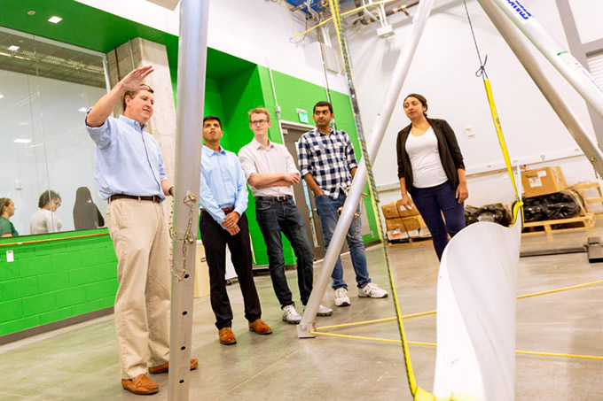 UT Dallas students are part of a team of researchers building a prototype of the turbine. Griffith (left) discusses the properties of a blade that will be used for a more traditional wind turbine design.