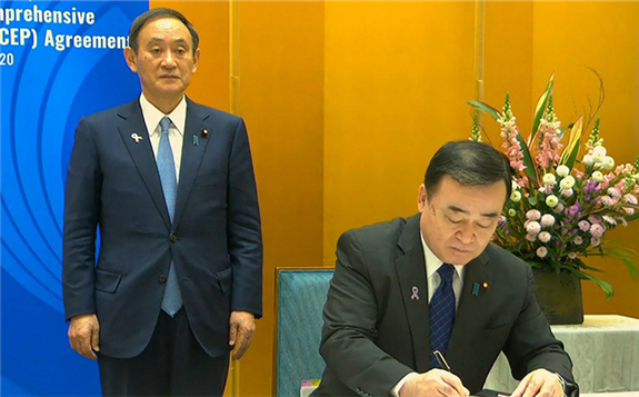 A screen grab taken from Vietnam Host Broadcaster's November 15, 2020 live video shows Japan's Prime Minister Yoshihide Suga (left) standing next to Japan's Minister of Economics, Trade and Industry Hiroshi Kajiyama as he signs the agreement during the signing ceremony for the Regional Comprehensive Economic Partnership (RCEP). Photo: AFP